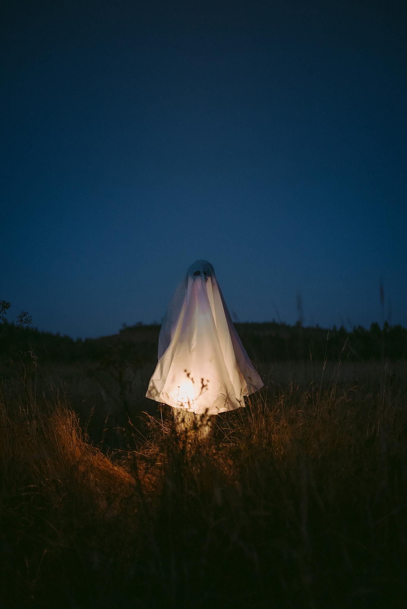 Illuminated ghostly figure draped in white shroud standing in a dimly lit field at night.